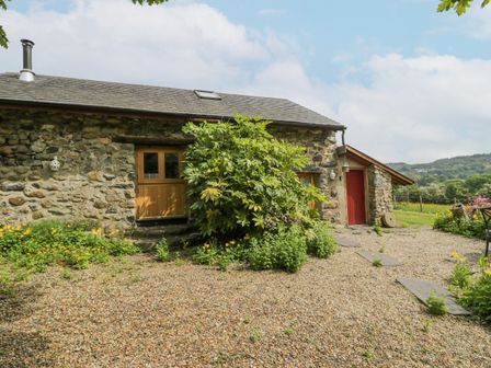 A stone cottage with wooden windows a red door and garden path with plants at The Shippon in Llechwedd The Conwy Valley