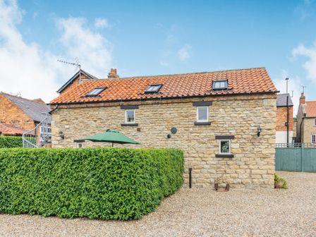 A stone house with a red tiled roof and three skylights surrounded by a hedge and gravel at Upstairs Downstairs Cottage in Snainton near Scarborough