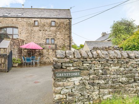 Stone building with small windows and outdoor table with pink umbrella behind a stone wall at Greystones Milton near Milnthorpe