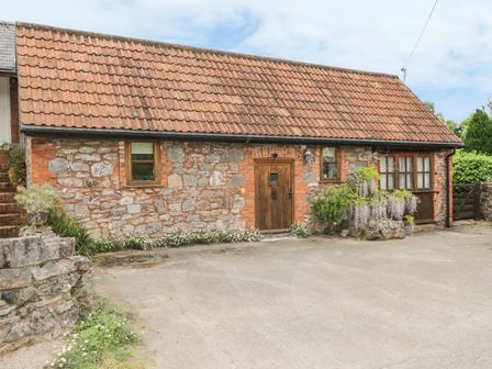 Exterior of a stone cottage with wooden door and windows surrounded by plants and flowers at High Park Barn in Uffculme Blackdown Hills