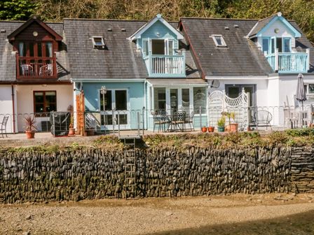 Three connected houses with balconies and outdoor seating on a stone embankment at Waterside Cottage in Little Petherick Creek near Padstow