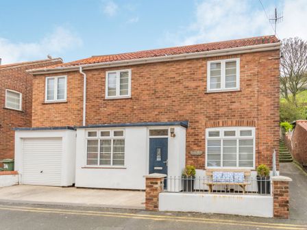 A brick house with white framed windows a garage and a bench with cushions at Quayside House in Scarborough