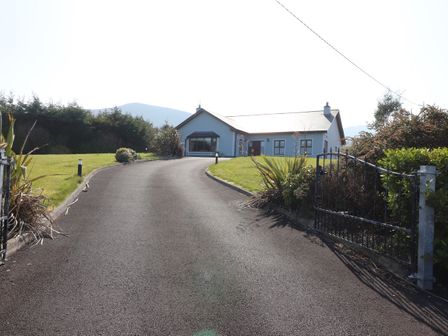 A driveway leading to a detached house with a black gate and surrounding greenery at Kissane's Cottage in Beaufort County Kerry