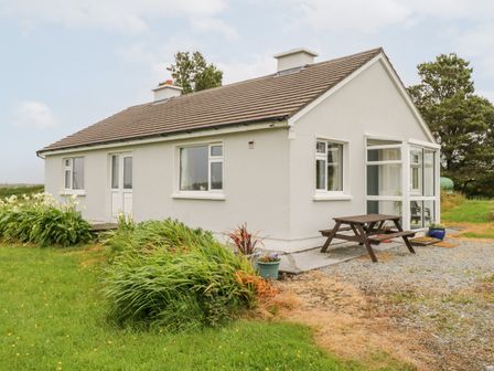 A single story house with white walls and a brown roof surrounded by grass and plants at Roundstone Bay View in Inishnee Island County Galway