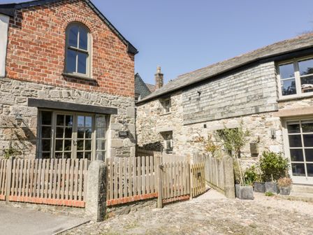 An exterior view of two connected stone and brick cottages with fenced patios and potted plants at The Old Smithy in St Columb Major near Newquay