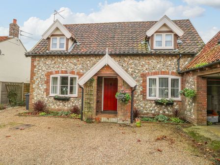 A stone cottage with two dormer windows a red front door and gravel driveway at Sleepeezy in Little Snoring