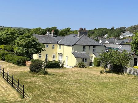 A yellow two story house with multiple chimneys surrounded by trees and grass at Gwelfor in Morfa Bychan