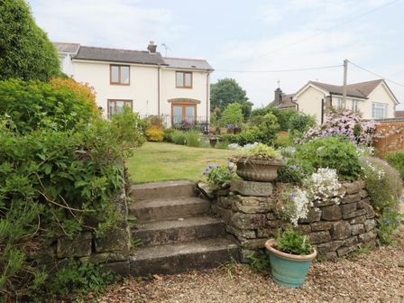 An outdoor garden area with stone steps leading to a lawn and two houses in the background at Lynton House in Ruardean Hill near Drybrook