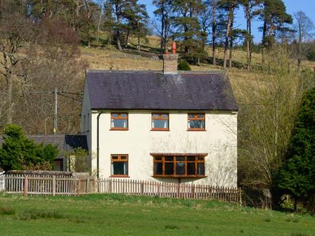 A two-story house with a fenced yard and trees on a hillside at Hartam House in Falstone near Kielder and Bellingham