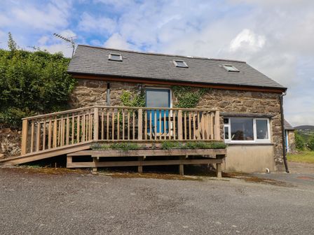 A stone house with a wooden balcony and blue door under a cloudy sky at The Grain Store in Abersoch
