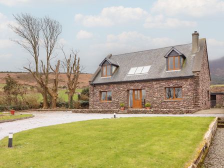 A stone house with a slate roof and wooden framed windows surrounded by grass and trees at Finn House in Castlegregory County Kerry