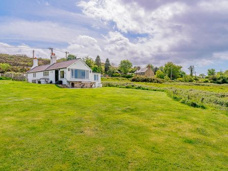 A white cottage with chimneys and large windows on a grassy lawn under a partly cloudy sky at Crown Cottage in Trelogan near Llanasa