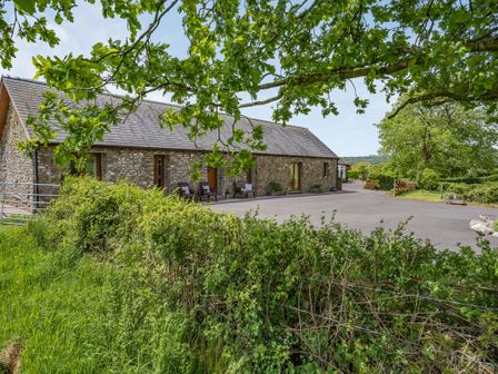 A stone barn style building with wooden doors and chairs outside surrounded by greenery at Ysgubor Hir in Pontarddulais near Swansea