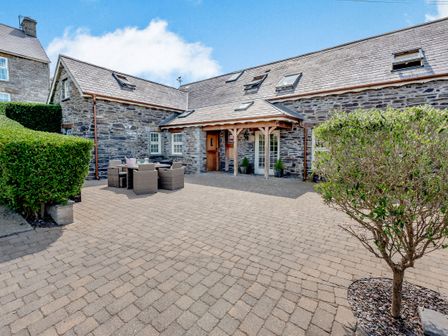 A stone building with a paved courtyard with outdoor seating and plants at Ysgubor Uchaf in Brongest near Newcastle Emlyn
