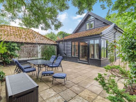 A patio with outdoor chairs and table next to a black wooden house at Ducksfoot Barn Bush Green near Pulham Market