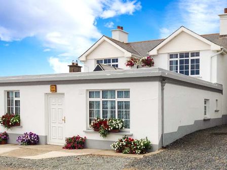 A white house with multiple windows and flower pots outside at Seascape in Fethard-On-Sea County Wexford