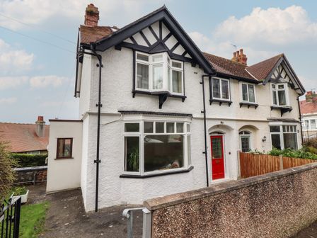 A semi detached white house with a red door and bay windows at Highgate in Llandudno