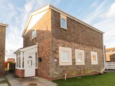 A brick house with a white front door and three small windows on one side a lawn and concrete path at Cheviot View in Beadnell