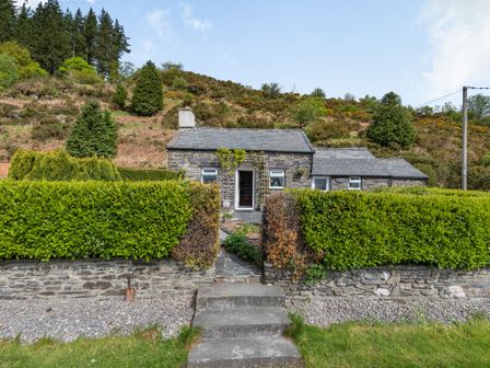 A stone cottage with steps leading to a garden gate and hedges at Henrhiw Bach in Penmachno