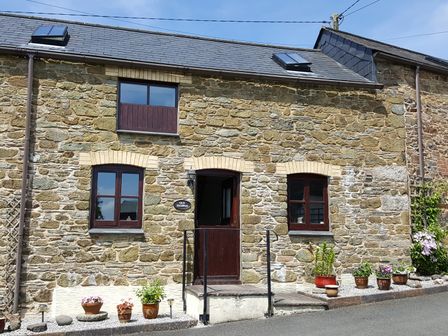 A stone house with dark wooden windows and door with plants in pots outside at The Shippon Near Launceston