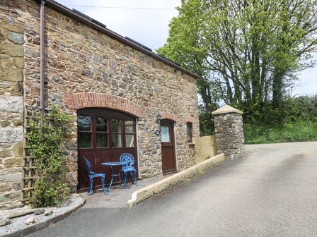 A stone building with a blue metal table and two chairs outside near a road at The Wagon House in Polyphant near Launceston