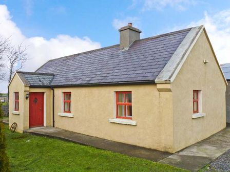 A single story house with a pitched roof red door and red window frames surrounded by grass at Cavan Hill Cottage in Ballinrobe County Mayo