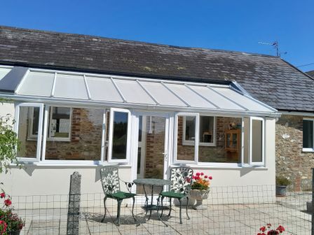 A patio with a metal table and two chairs outside a building with white framed windows and a glass door at 1 Cowdea Farm in Bettiscombe near Beaminster and Bridport