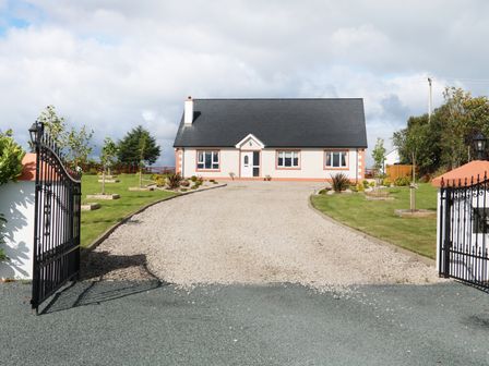 A house with a black roof and white walls at the end of a gravel driveway with iron gates and green lawns at Sallywood House Carn near Ballybofey County Donegal