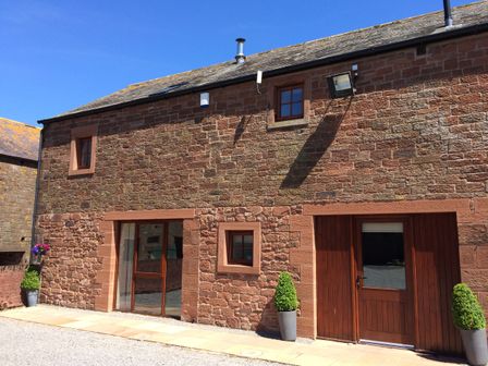 Exterior of a stone building with wooden doors and windows with potted plants outside at The Old Grainstore in Bolton Low Houses near Wigton