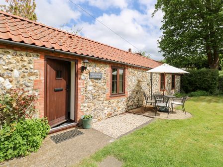 A stone cottage with a red tiled roof and outdoor table with umbrella in a garden at Moonlight Cottage in Coltishall
