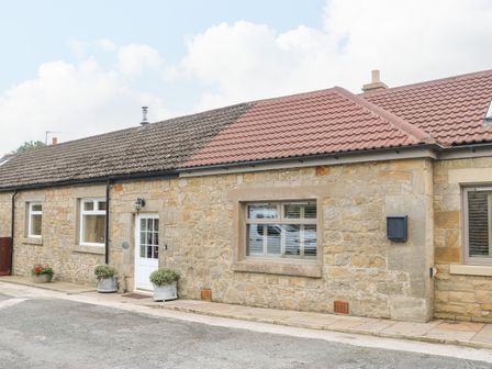 A stone cottage with white door and windows and potted plants outside at Stable Cottage in Belford near Bamburgh