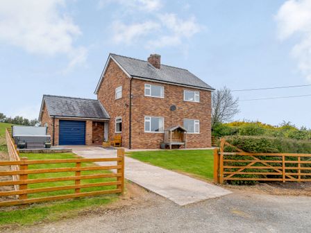 A two-story brick house with a blue garage door a wooden fence and a driveway at Pen Y Gaer Llannefydd near Abergele and Denbigh