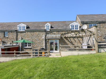 A stone house with dormer windows a green umbrella and wooden pergola on a lawn at Mill Cottage in Aberaeron