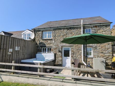 An outdoor patio area with a hot tub a wooden fence a picnic table with a large green umbrella and a stone house in the background at The Stable in Aberaeron