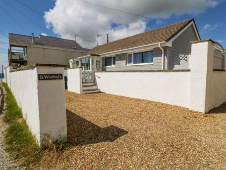 A bungalow with white walls and a gravel driveway at St Winifreds in Rhosneigr