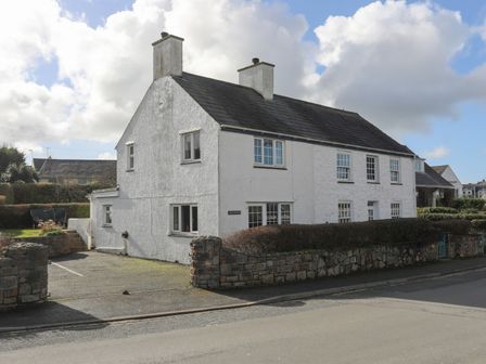 A white two chimney house with a grey roof and multiple windows beside a stone wall and road at Glan Y Don Bach in Abersoch