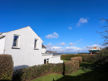 A white house with windows surrounded by bushes and lawn with a boat on a trailer and sea in the background at Glan Y Don in Abersoch