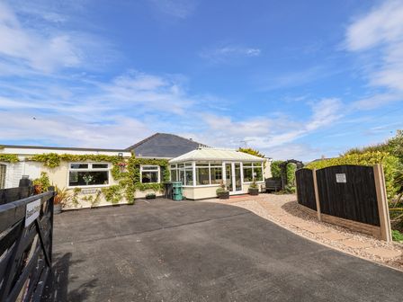 A single-story house with a conservatory and driveway at Beach Cottage in Conwy