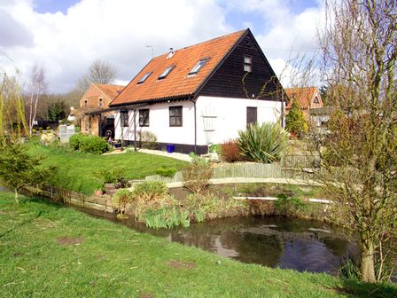 A house with a red roof near a small pond surrounded by grass and trees at The Hayloft in Necton near Swaffham