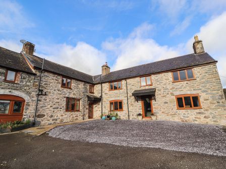Stone farmhouse with multiple windows and two doors under a blue sky at Maestyddyn Farm House in Clawddnewydd near Ruthin