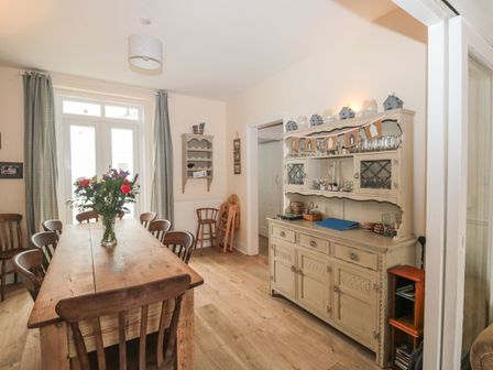 A dining room with a wooden table and chairs a cabinet with glassware and decorations and a vase with flowers on the table at Dunholme House in Teignmouth
