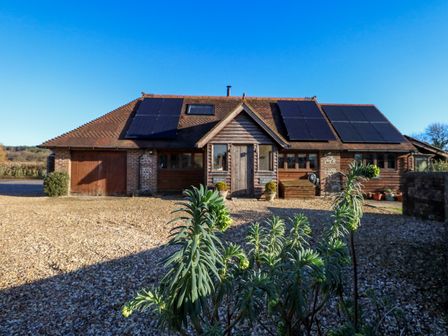 A house with solar panels on the roof and a gravel driveway with plants in the foreground at The Old School Cottage in Tincleton near Dorchester