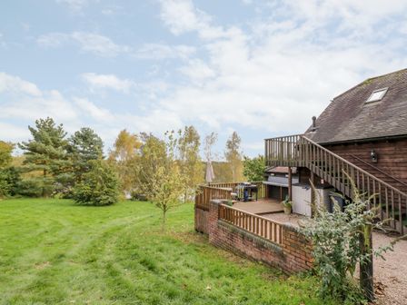 A backyard with grass trees a wooden deck with a barbecue and stairs at The Stilehouse Apartment in Menith Wood