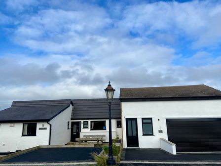 A white house with black windows and doors a wooden bench and a street lamp in front at Minerva in Trearddur Bay