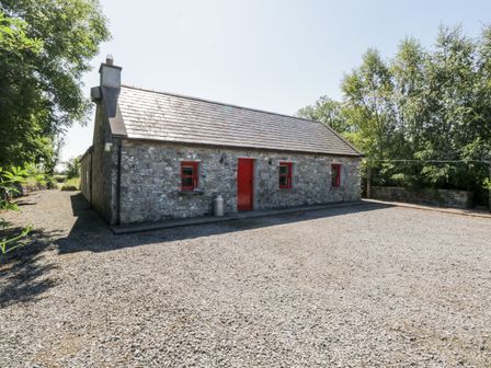 A stone cottage with red door and windows surrounded by trees and gravel at The Visiting House in Gorteen near Dunmore County Galway