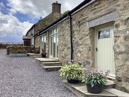 Stone exterior of a house with a door windows potted plants bench and gravel ground at Y Bwthyn in Ysbyty Ifan