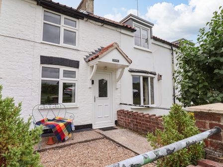 The exterior of a white house with a white door and windows a metal bench with a colorful blanket and small garden at The Cottage Kilham near Driffield
