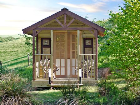 A small wooden cabin with two chairs on the porch in a grassy area at Cwm Derw Cottage in Llanafan Fawr near Builth Wells