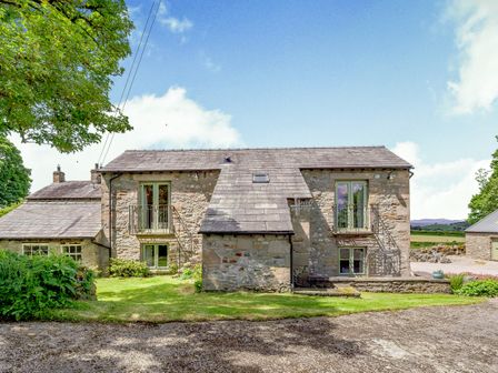 Stone house with slate roof and small balconies on the upper windows surrounded by grass and trees at Pickle Barn Hutton Roof near Kirkby Lonsdale