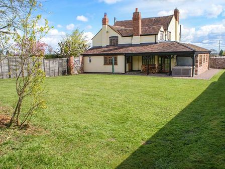 A large backyard with green grass a small tree and a house with patio furniture at Brambles Cottage in Little Malvern near Malvern